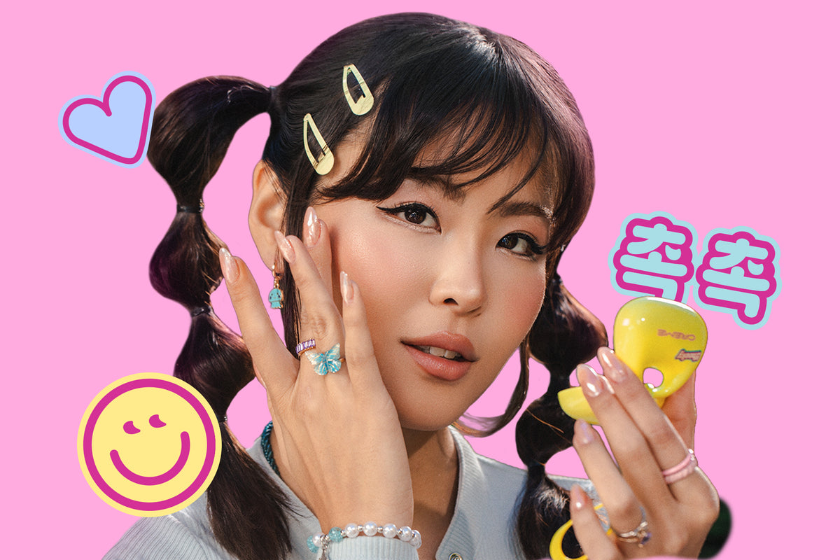 Model holding a yellow compact mirror against a pink background with playful heart and smiley graphics.